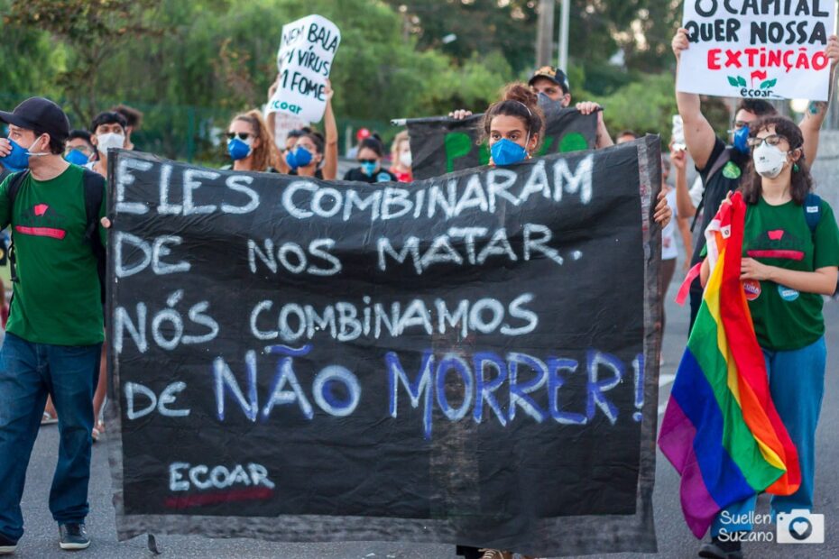 Militantes do Ecoar participam de um ato e seguram uma faixa em que se lê "Eles combinaram de nos matar. Nós combinamos de não morrer - Ecoar". Uma militante segura uma bandeira LGBT e, atrás dela, ouutro militante segura um cartaz, em que está escrito "O capital quer a nossa extinção - Ecoar".