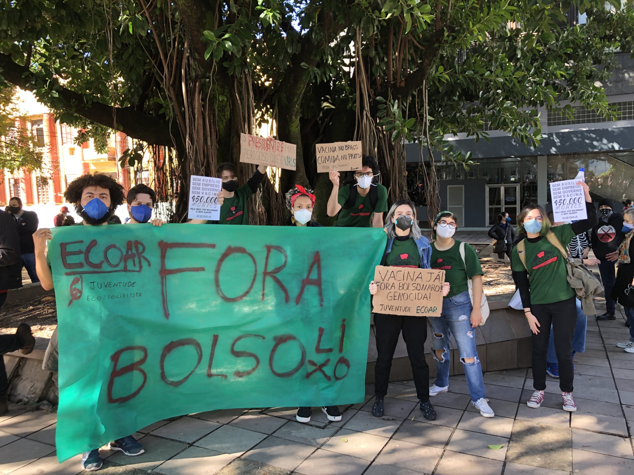 Imagem retangular em formato paisagem. 8 militantes com camisetas verdes do coletivo Ecoar posam para a foto, segurando cartazes. Em destaque, está uma faixa verde em que está escrito "Fora BolsoLixo".