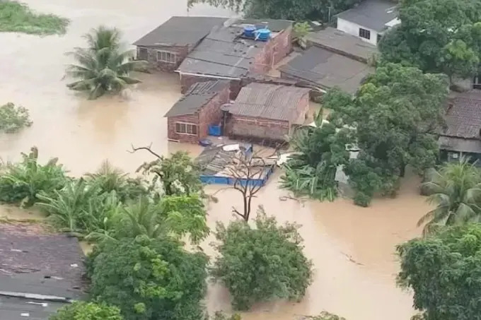 Imagem retangular em formato paisagem. A imagem é uma foto aérea, se veem algumas casas e árvores cobertas pela enchente.