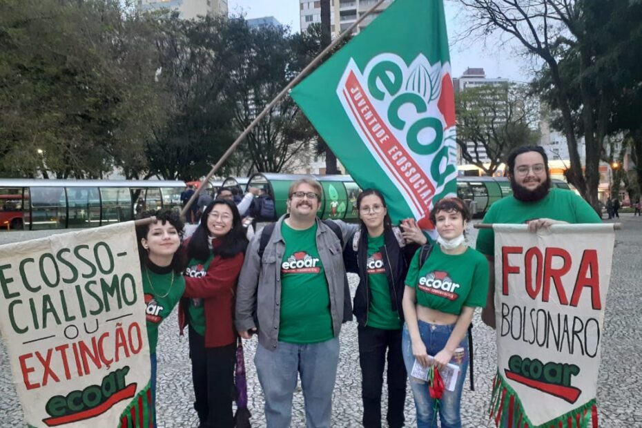 7 militantes vestindo camisetas verdes do Ecoar seguram estandartes e uma bandeira do coletivo