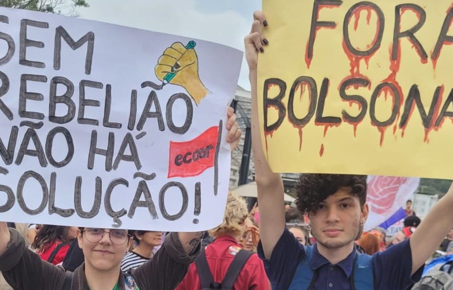 Dois militantes seguram cartazes. No primeiro, está escrito "Sem rebelião não há revolução" e, no segundo "Fora Bolsonaro"